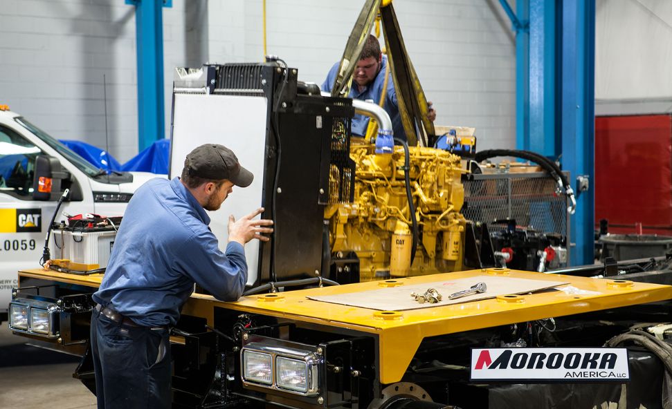 Two workers assemble heavy machinery at Morooka America’s U.S. manufacturing facility.